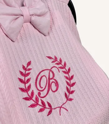 Pembe örgü pike kumaştan, fırfırlı kenarlara sahip, fiyonklu kapaklı puset örtüsü.
